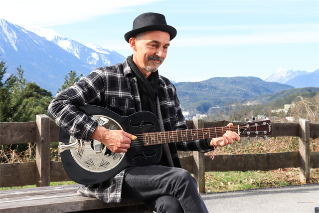 Frajo Köhle sitzt auf einer Bank am Birkenberg und spielt Gitarre. Er lächelt.